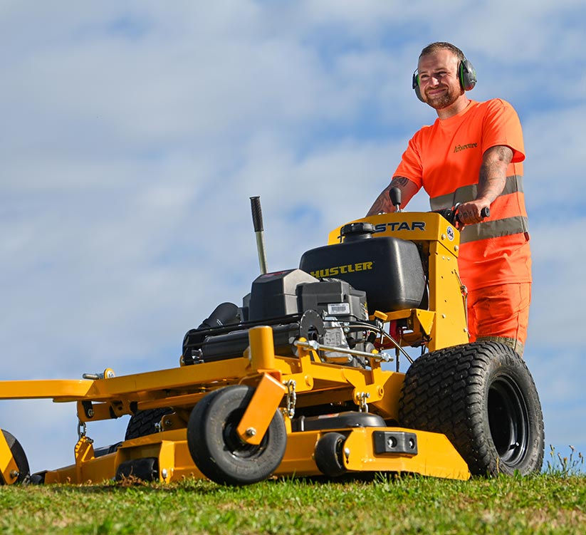 Arborcure employee in orange high visibility uniform mowing grass with industrial law mower